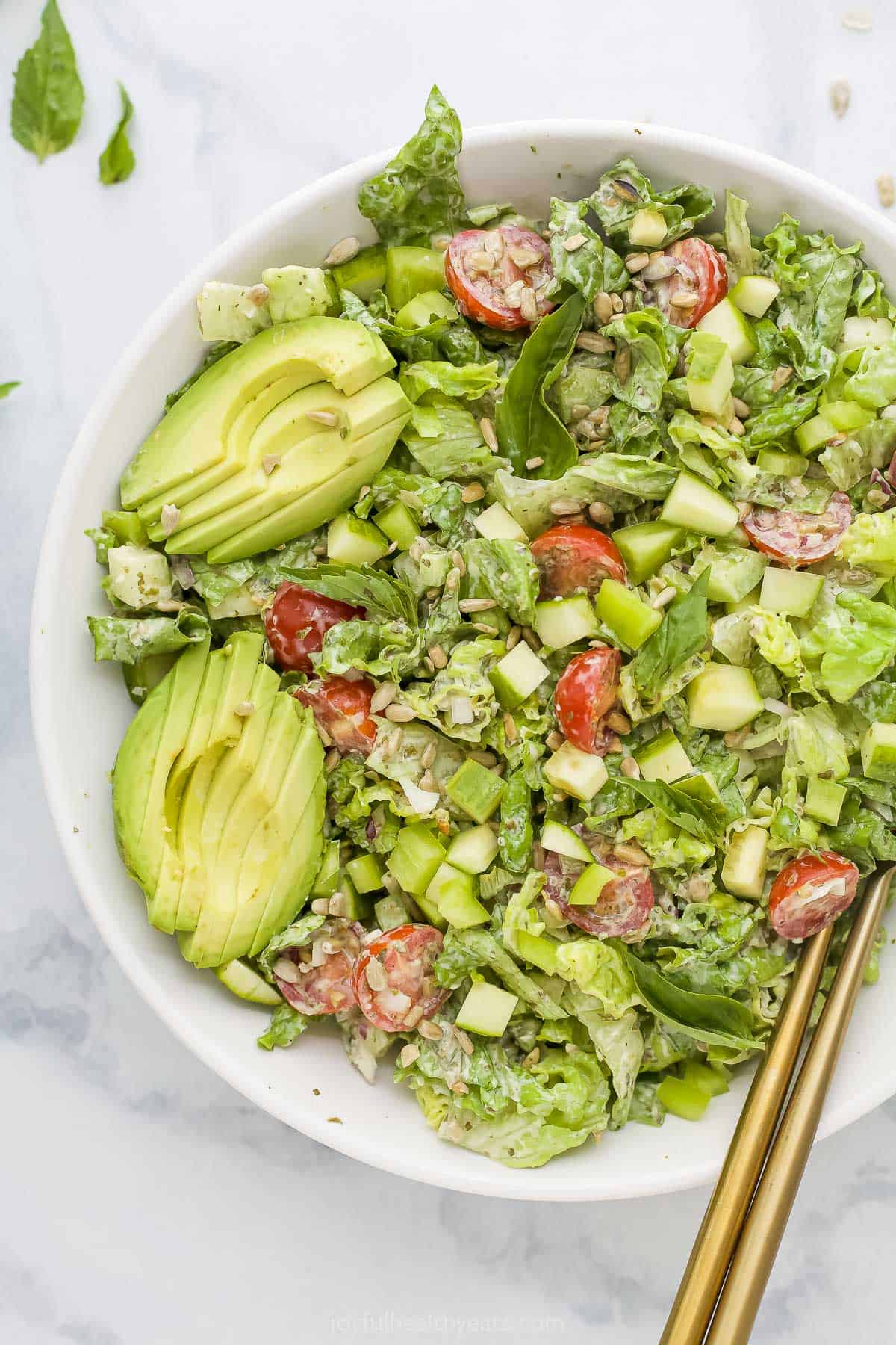 A pair of golden chopsticks digging into a bowl of green goddess salad