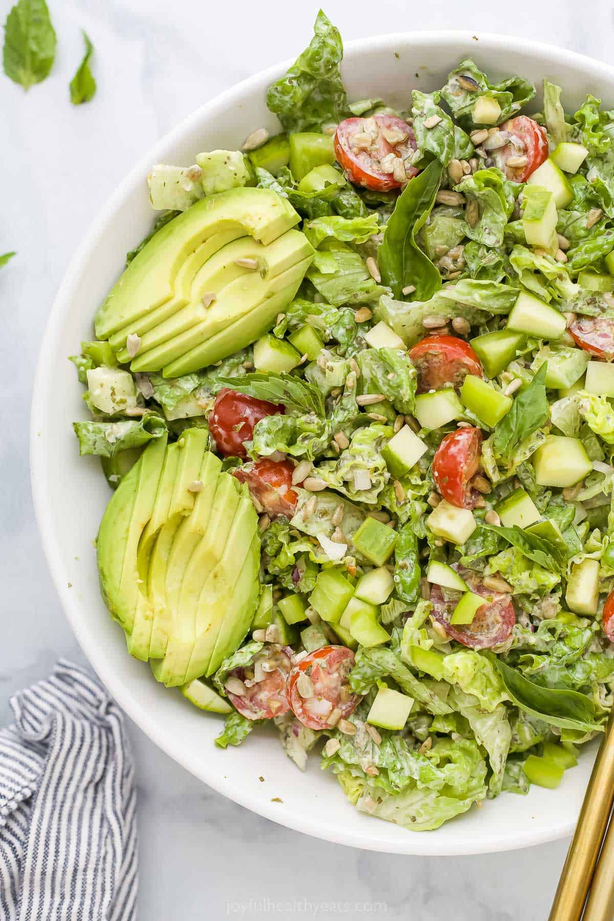 A close-up shot of green goddess salad in a bowl with a striped kitchen towel next to it