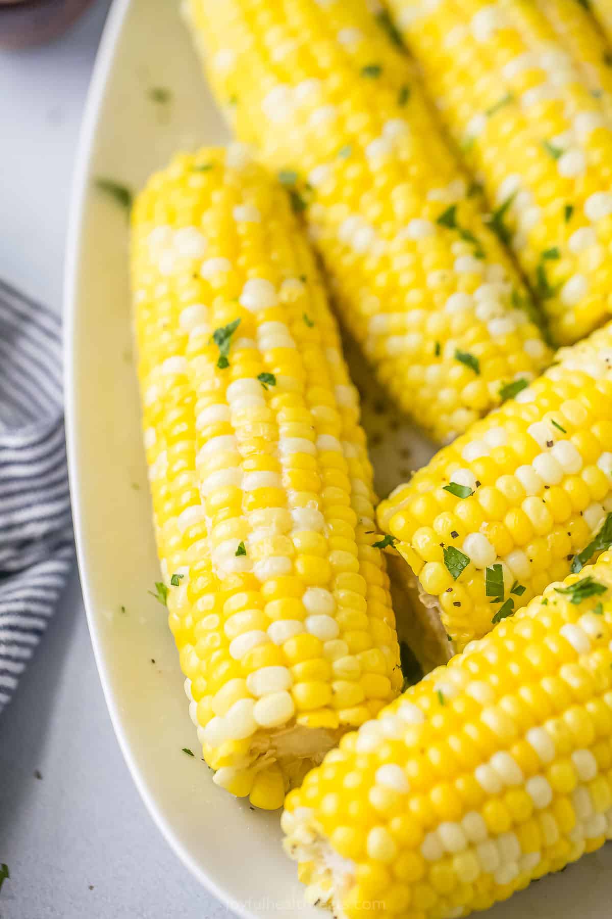 Instant Pot corn on the cob on a white serving platter beside a striped dishtowel