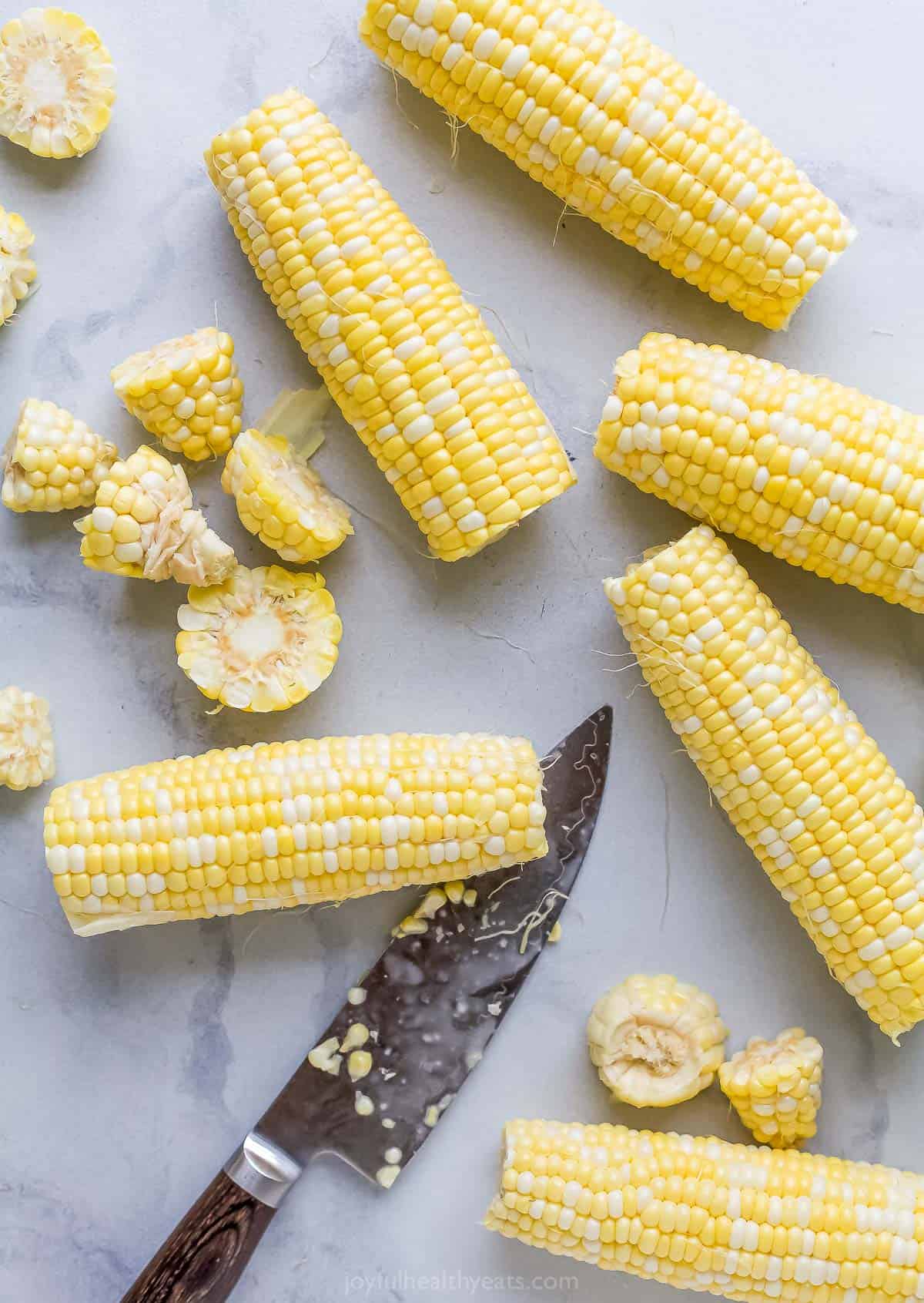 Trimmed corn on the cob on a kitchen countertop with a sharp chef's knife