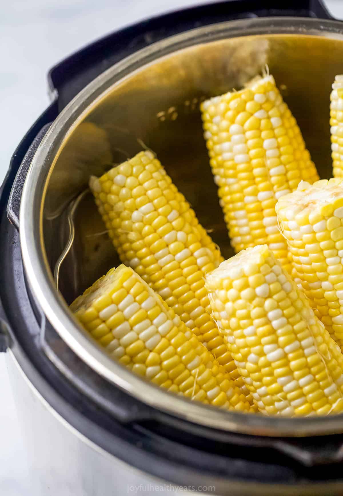 Six shucked and trimmed ears of corn sitting upright in a pressure cooker