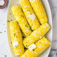 A serving platter full of cooked corn on the cob on top of a marble surface