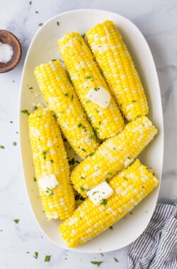 A serving platter full of cooked corn on the cob on top of a marble surface