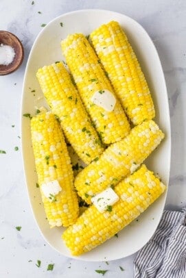 A serving platter full of cooked corn on the cob on top of a marble surface