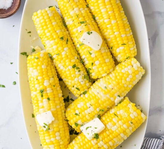 A serving platter full of cooked corn on the cob on top of a marble surface