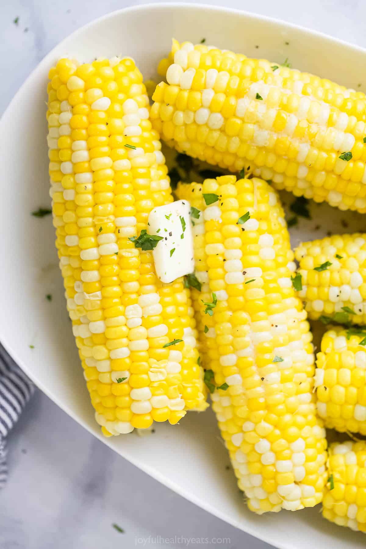 Pressure cooker corn on the cob topped with a pat of butter and a sprinkle of chopped herbs