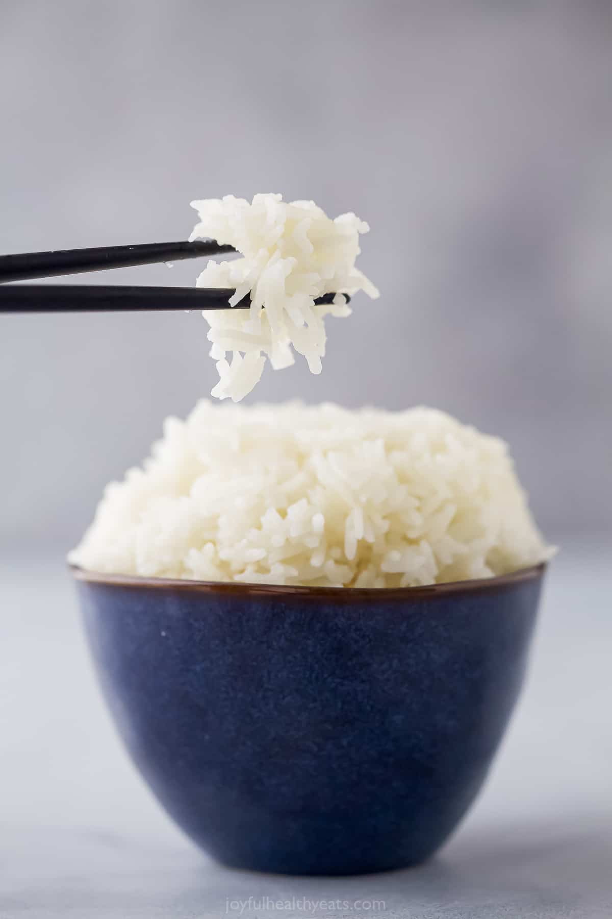 a small blue bowl with cooked white rice and chopsticks taking a bit out