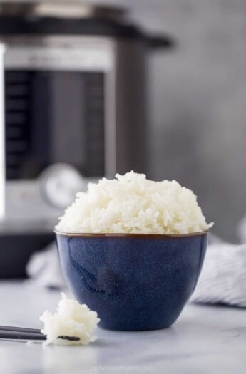 A bowl of Jasmine rice with chopsticks on a countertop