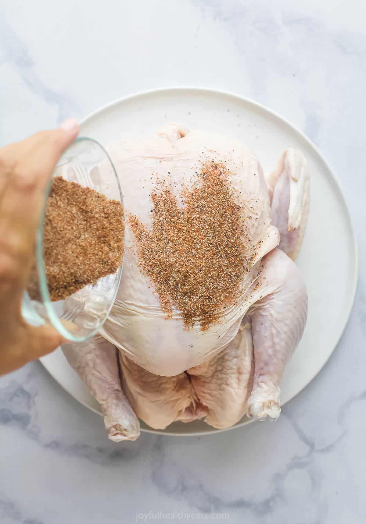 a person pouring dried seasonings onto a whole chicken