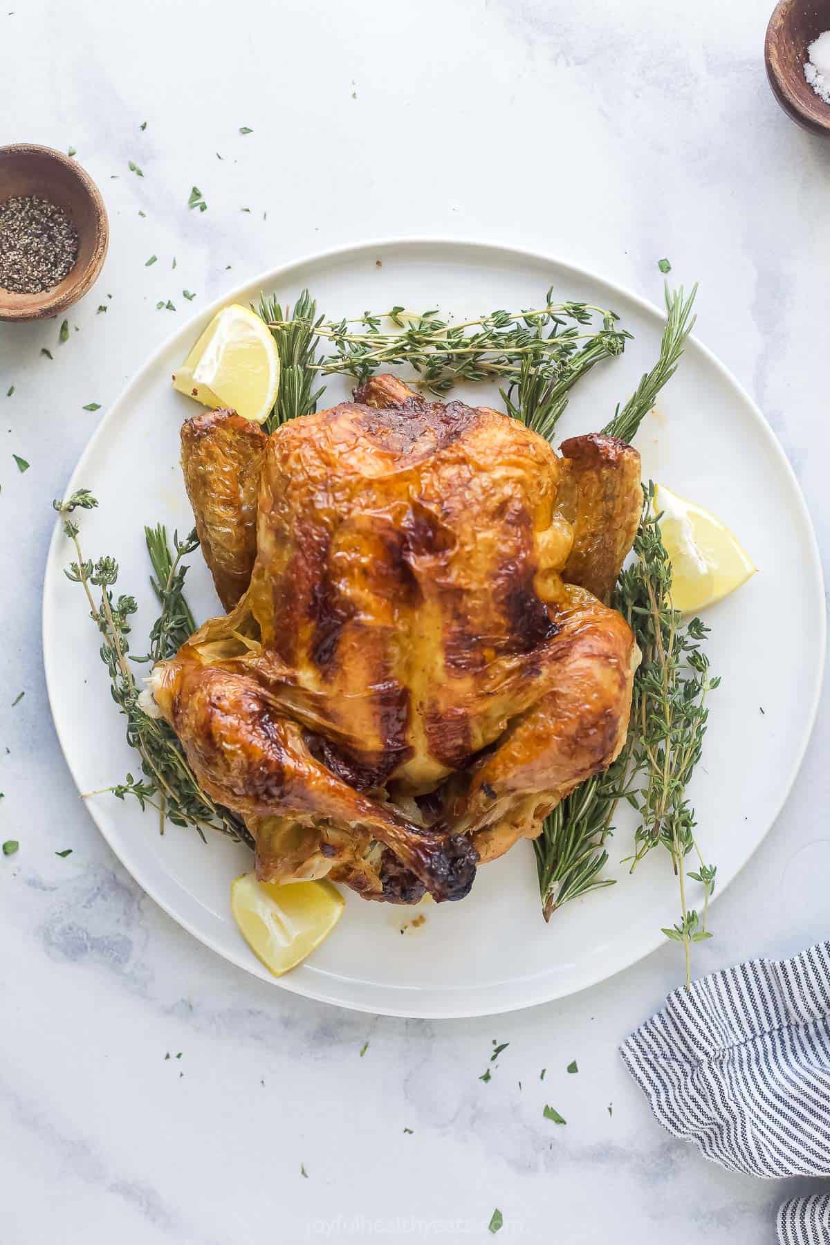 a roasted whole chicken on a platter with fresh herbs and lemon wedges