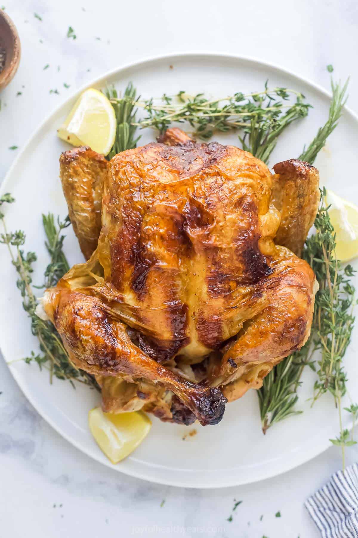 a roasted whole chicken on a platter with fresh herbs and lemon wedges