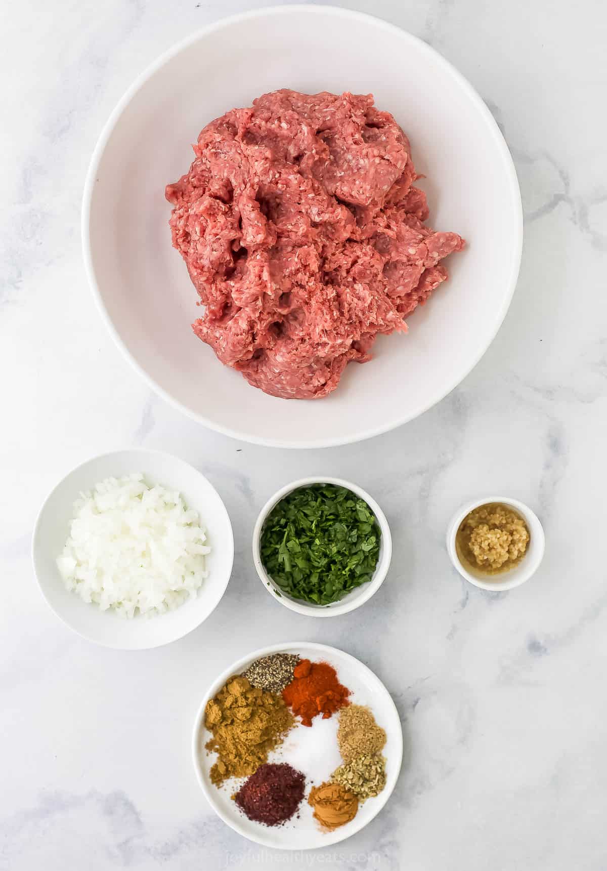 Ground meat, minced garlic, finely diced onions and the rest of the kabob ingredients on a countertop