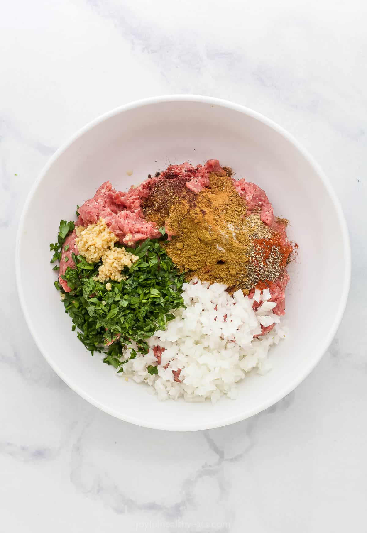 Finely ground beef in a bowl with chopped onions, minced garlic and a Middle Eastern spice blend