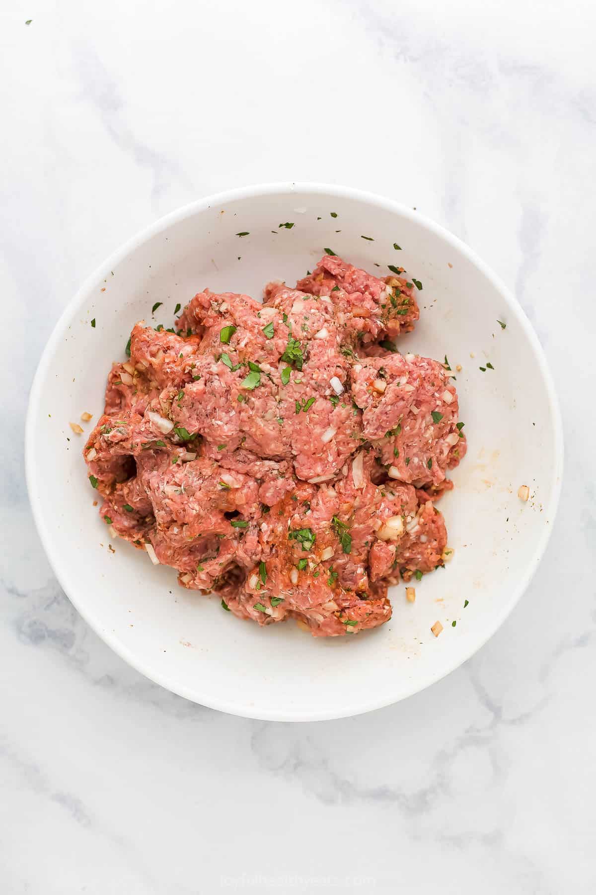 The ground beef mixture in a white bowl on a marble kitchen counter