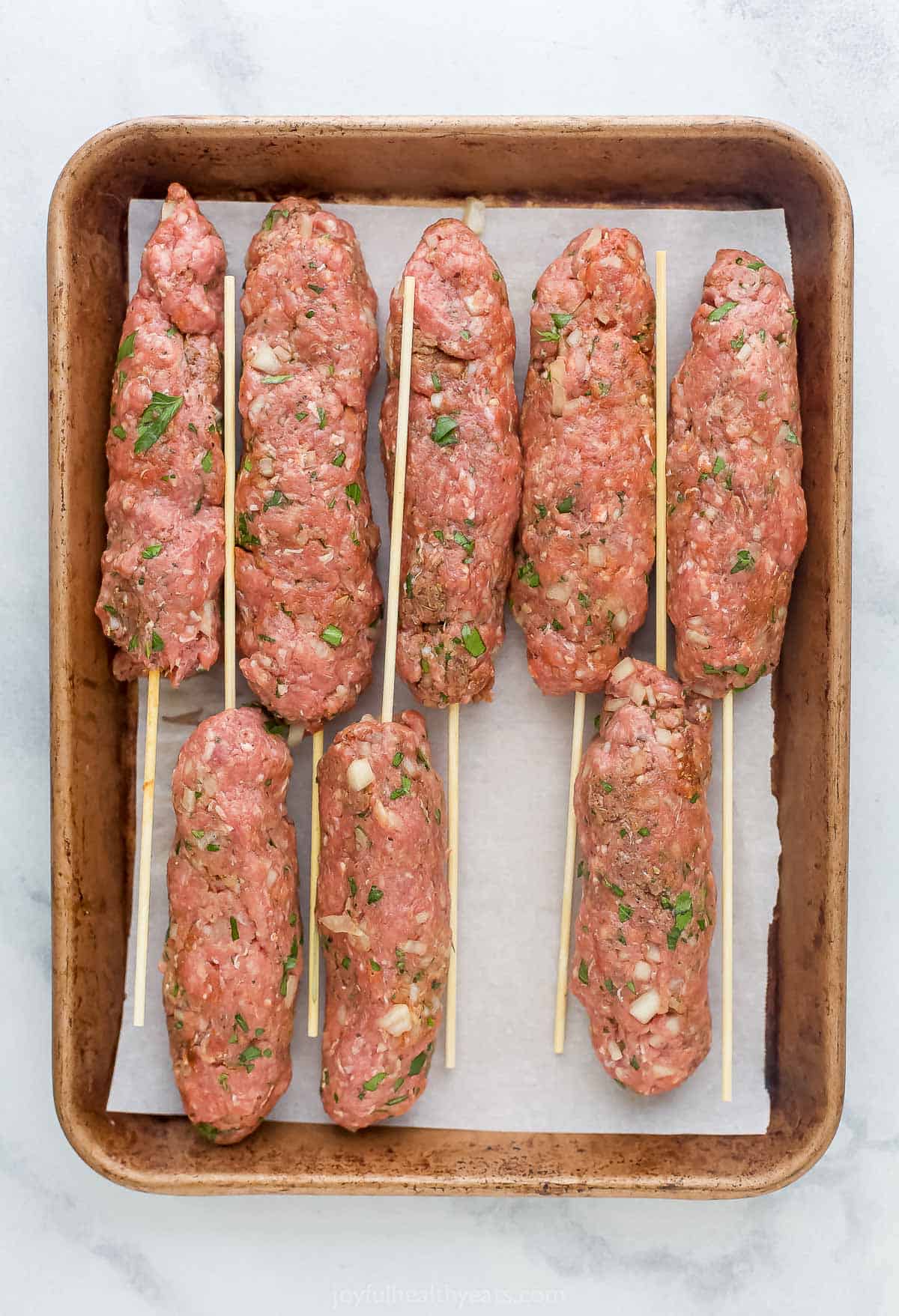 Eight raw kefta kabobs on a baking sheet lined with parchment paper