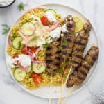 A plate of kefta on a marble kitchen countertop beside a bowl of tzatziki sauce