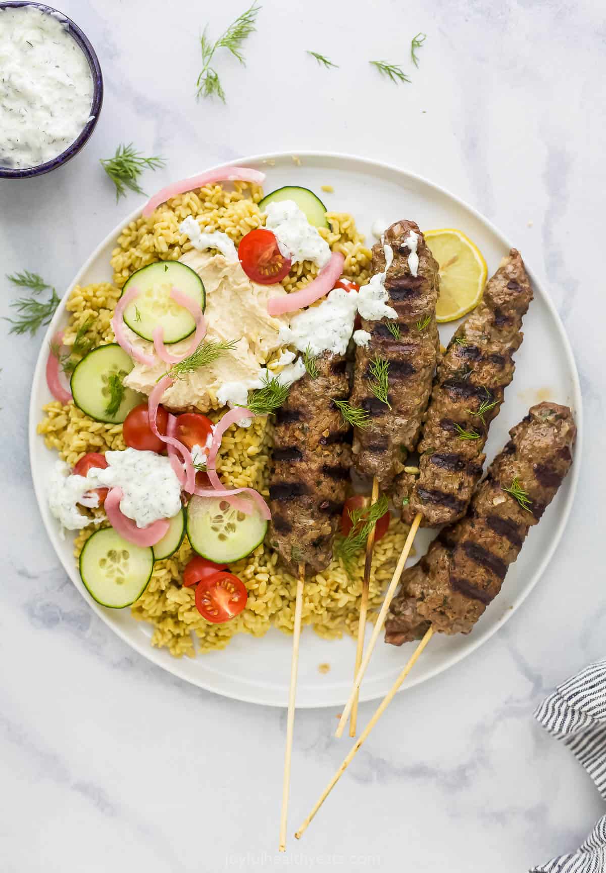 A plate of kefta on a marble kitchen countertop beside a bowl of tzatziki sauce