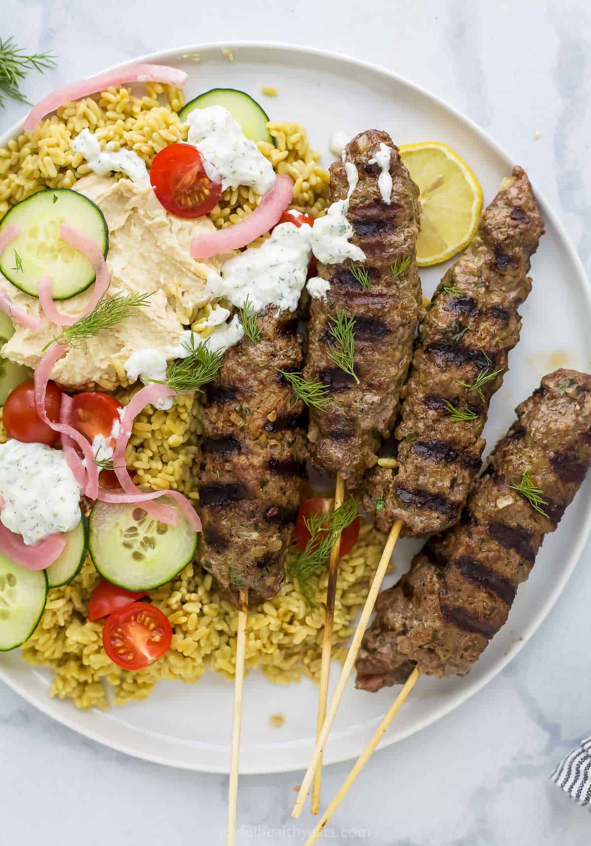 Kefta kabobs on a plate with rice, veggies, tzatziki and hummus