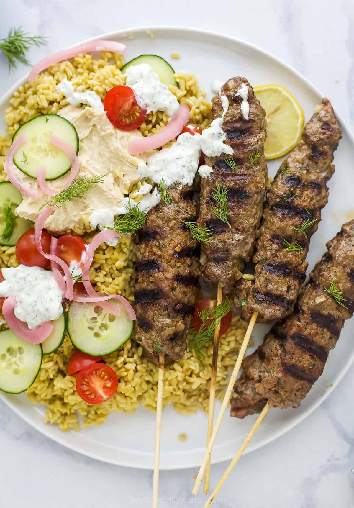 A plate full of kefta, rice, cucumbers, tomato and tzatziki sauce