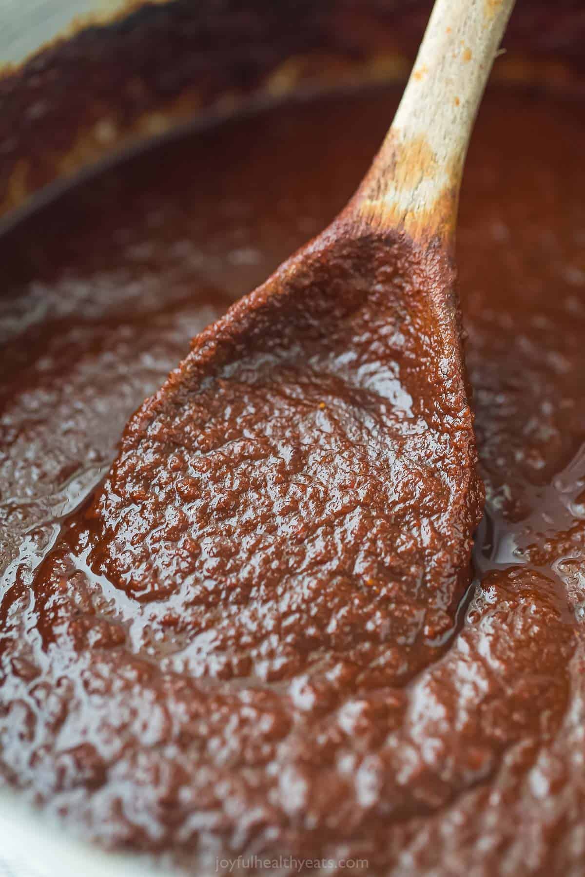 close up of a spoon with red enchilada sauce being stired in a pot