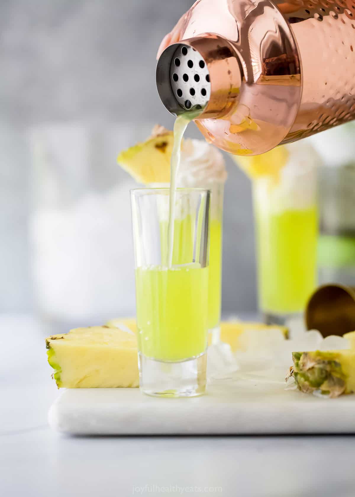a lime green colored cocktail being poure dinto a shot glass