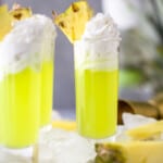 A Scooby Do Shot which is a a lime green colored cocktail in a tall shot glsas with whipped cream and pineapple garnish