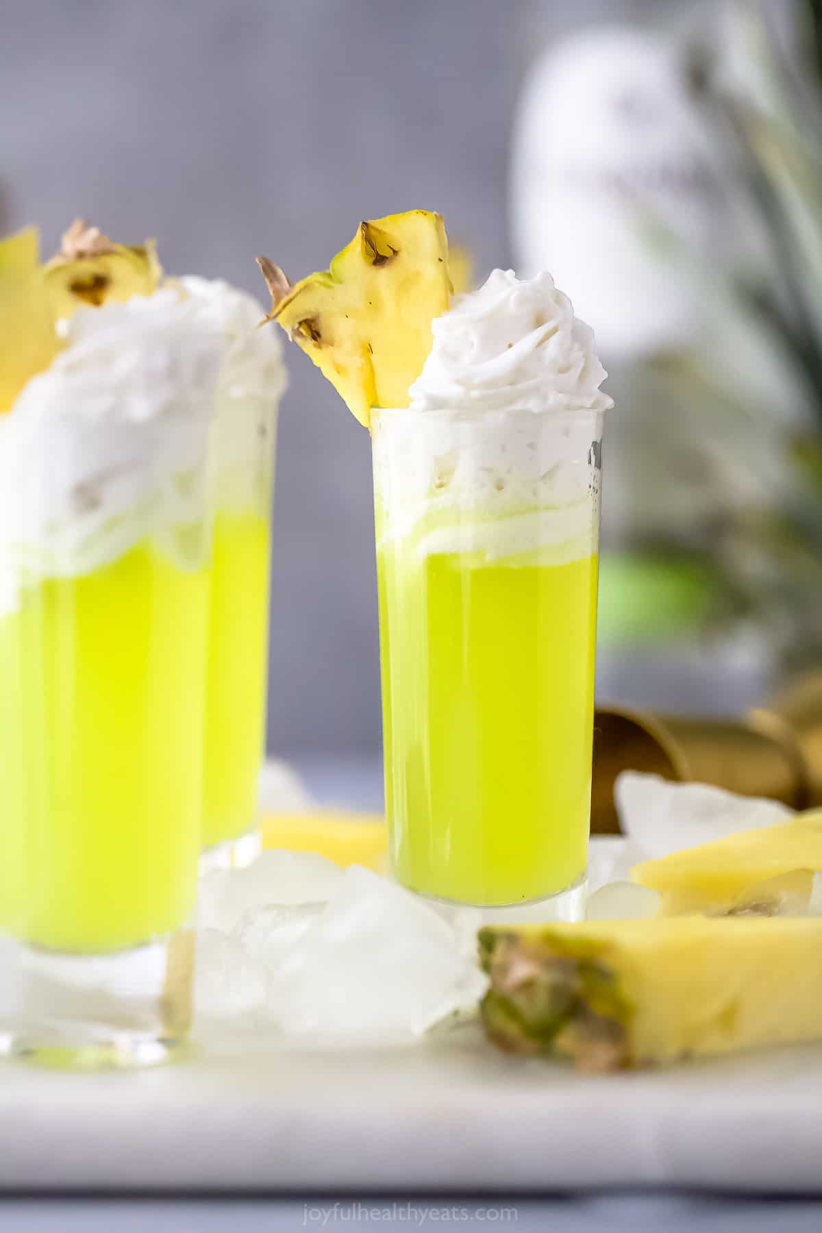 A Scooby Do Shot which is a a lime green colored cocktail in a tall shot glsas with whipped cream and pineapple garnish