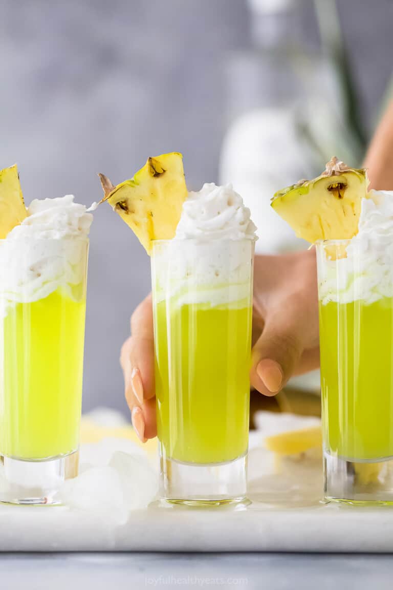 a lime green colored cocktail in a tall shot glsas with whipped cream and pineapple garnish