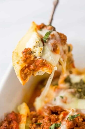 A spoon lifting a ricotta stuffed shell from a baking dish full of stuffed shells