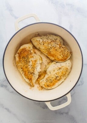 Three chicken breasts being cooked in a large dutch oven.