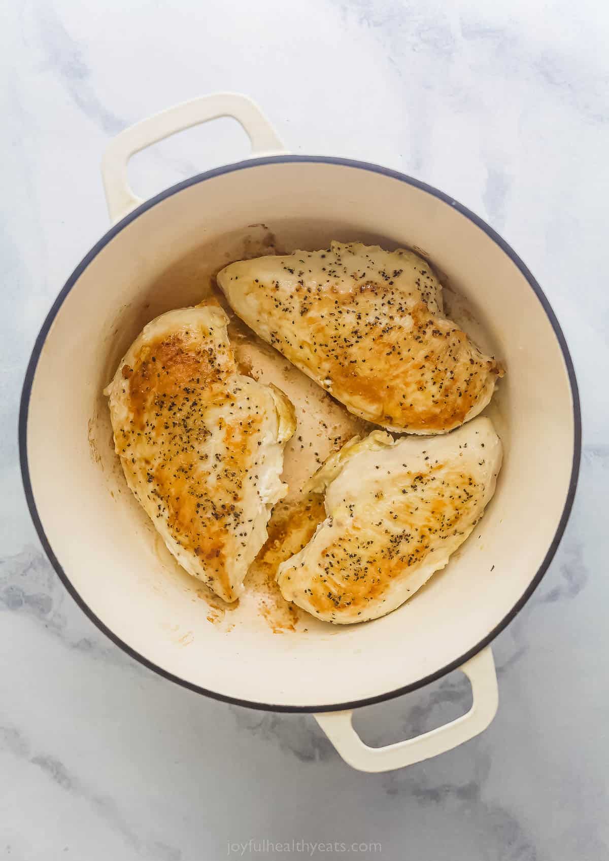 three chicken breasts being cooked in a large dutch oven