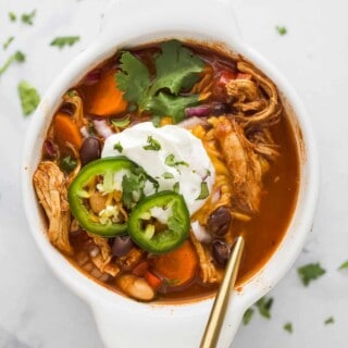 a bowl of smoky chicken chili with sliced jalapenos, sour cream, and cilantro