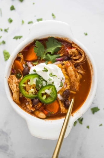 a bowl of smoky chicken chili with sliced jalapenos, sour cream, and cilantro