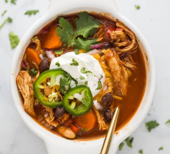 a bowl of smoky chicken chili with sliced jalapenos, sour cream, and cilantro