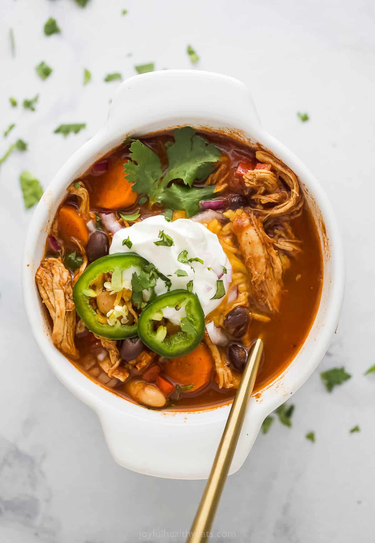 A bowl of smoky chicken chili with sliced jalapenos, sour cream, and cilantro.