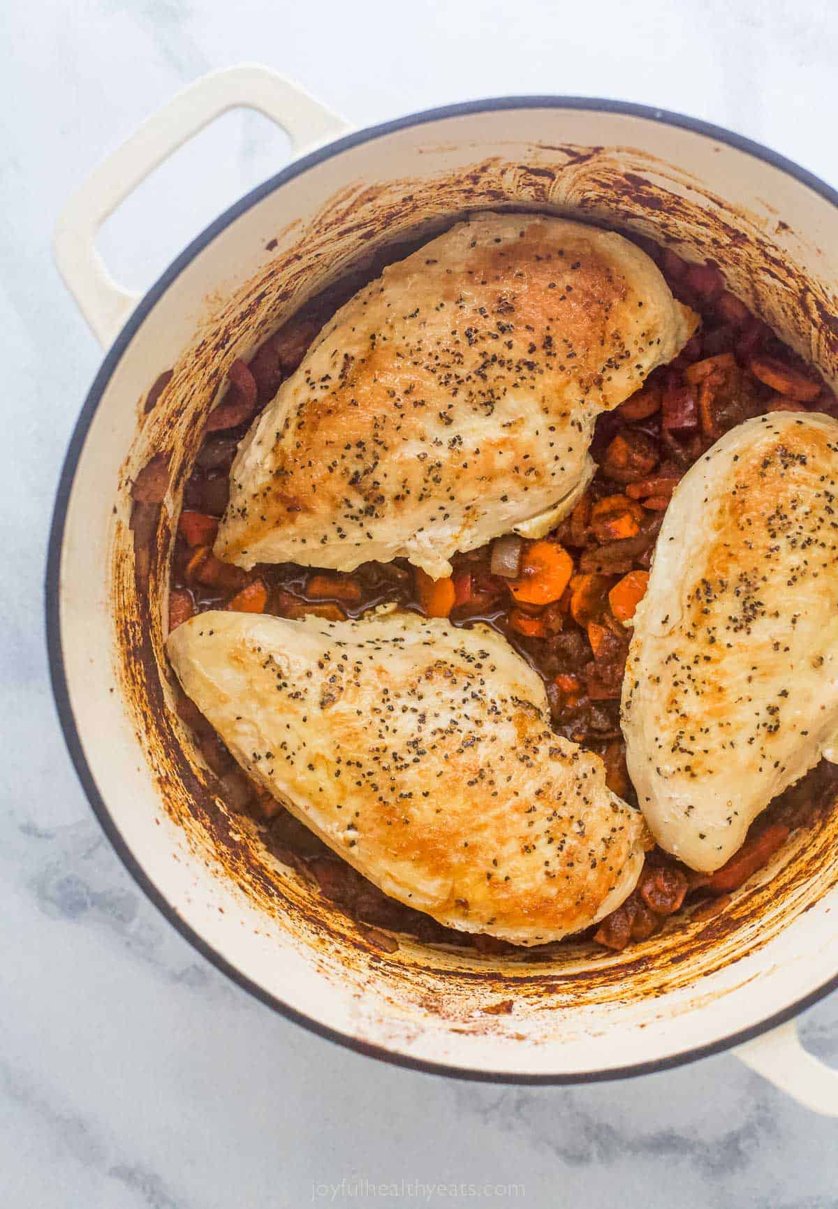 three chicken breasts cooked in a large pot with vegetables and a tomato based sauce