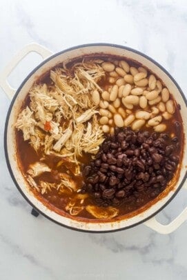 A large pot with beans, chicken, and tomato-based broth.