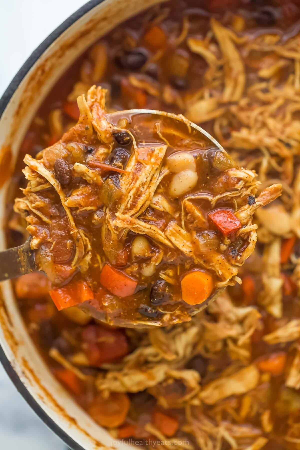 a ladle full of chili over a ، of chicken chili