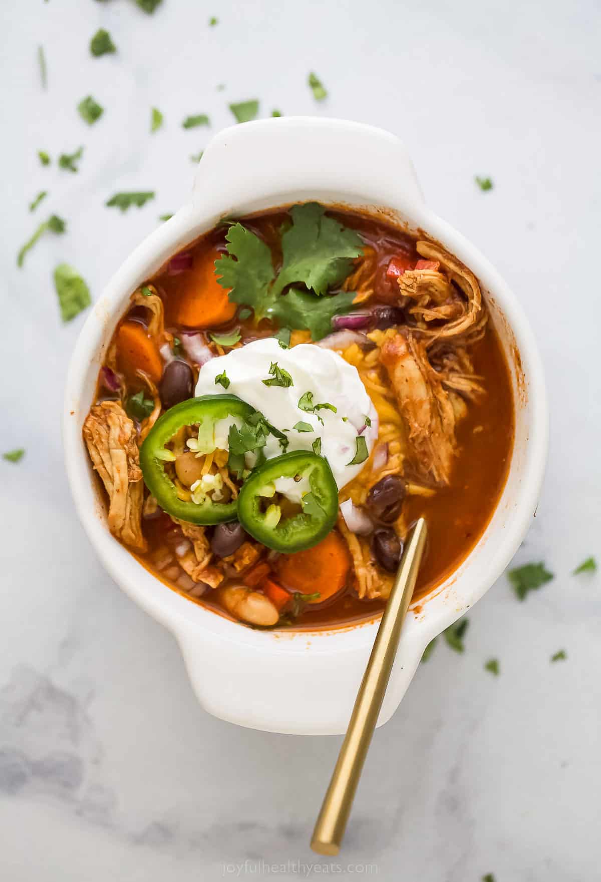 a bowl of smoky chicken chili with sliced jalapenos, sour cream, and cilantro