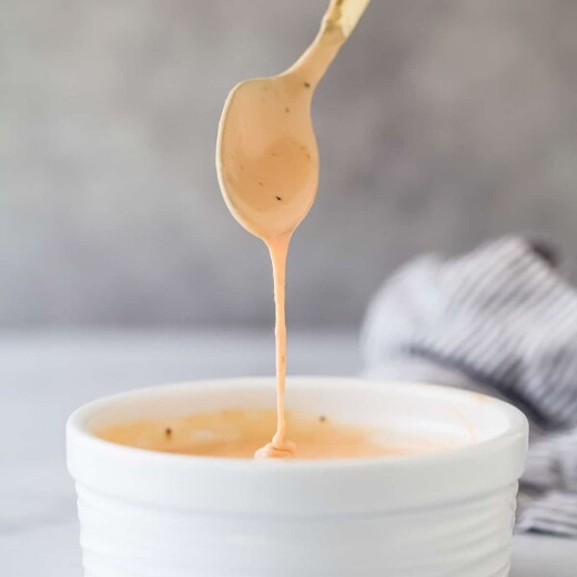 a spoon coming out of a small ramekin of a pale pink mayonnaise based sauce