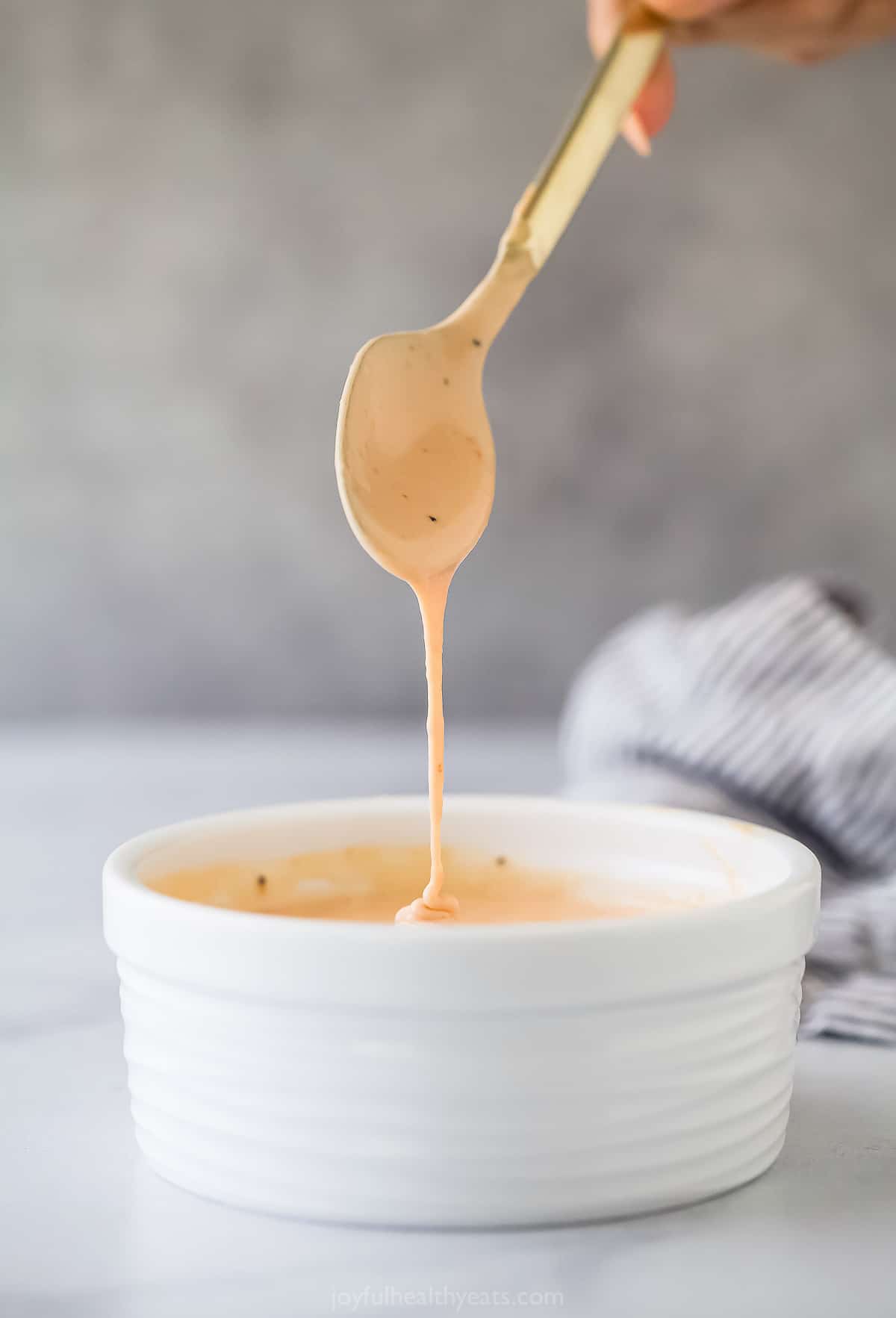 a spoon coming out of a small ramekin of a pale pink mayonnaise based sauce
