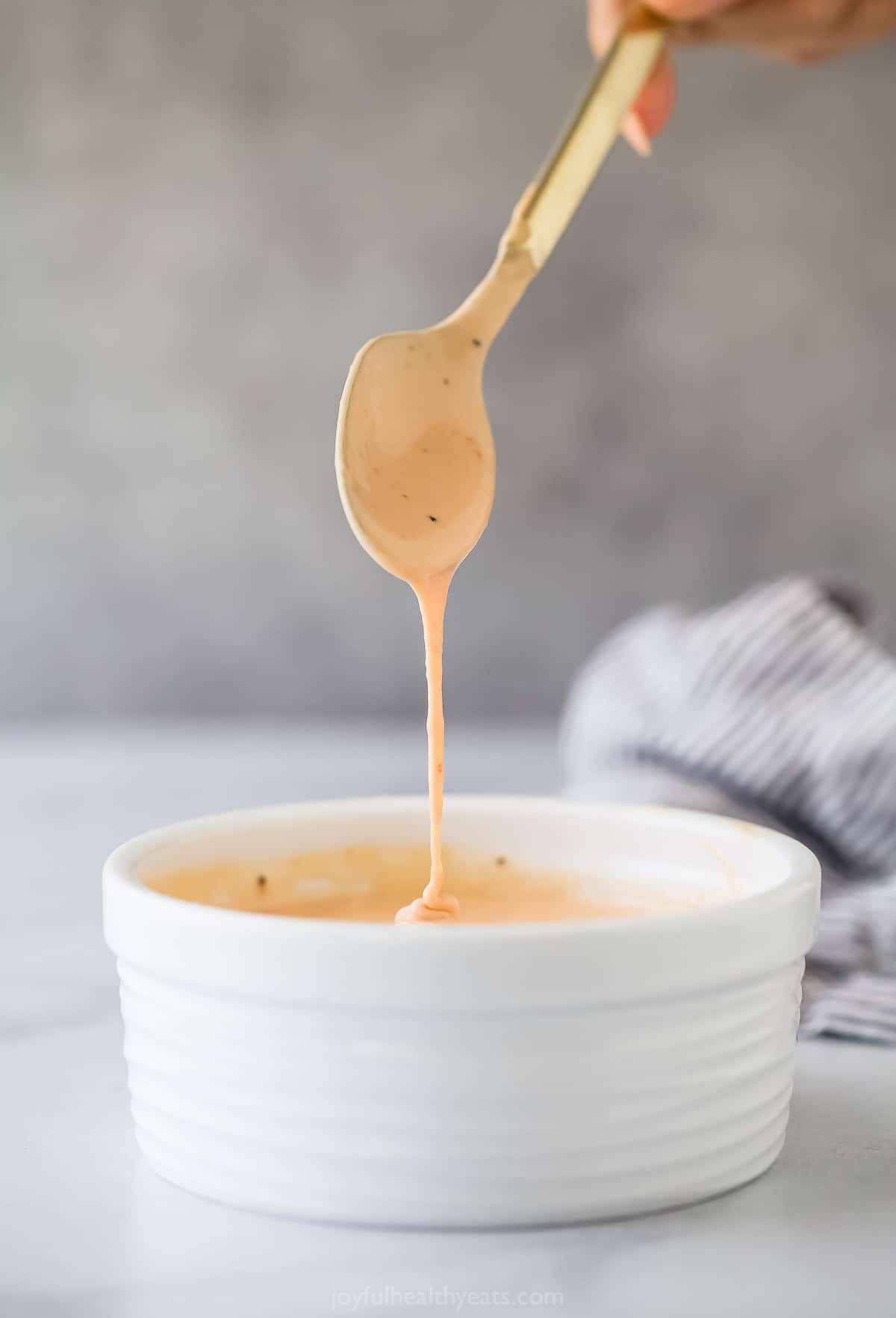 Here's how to make Boom Boom Sauce right at home. This super easy sauce is made with mayo, chili sauce, ketchup, and sriracha. a spoon coming out of a small ramekin of a pale pink mayonnaise based sauce