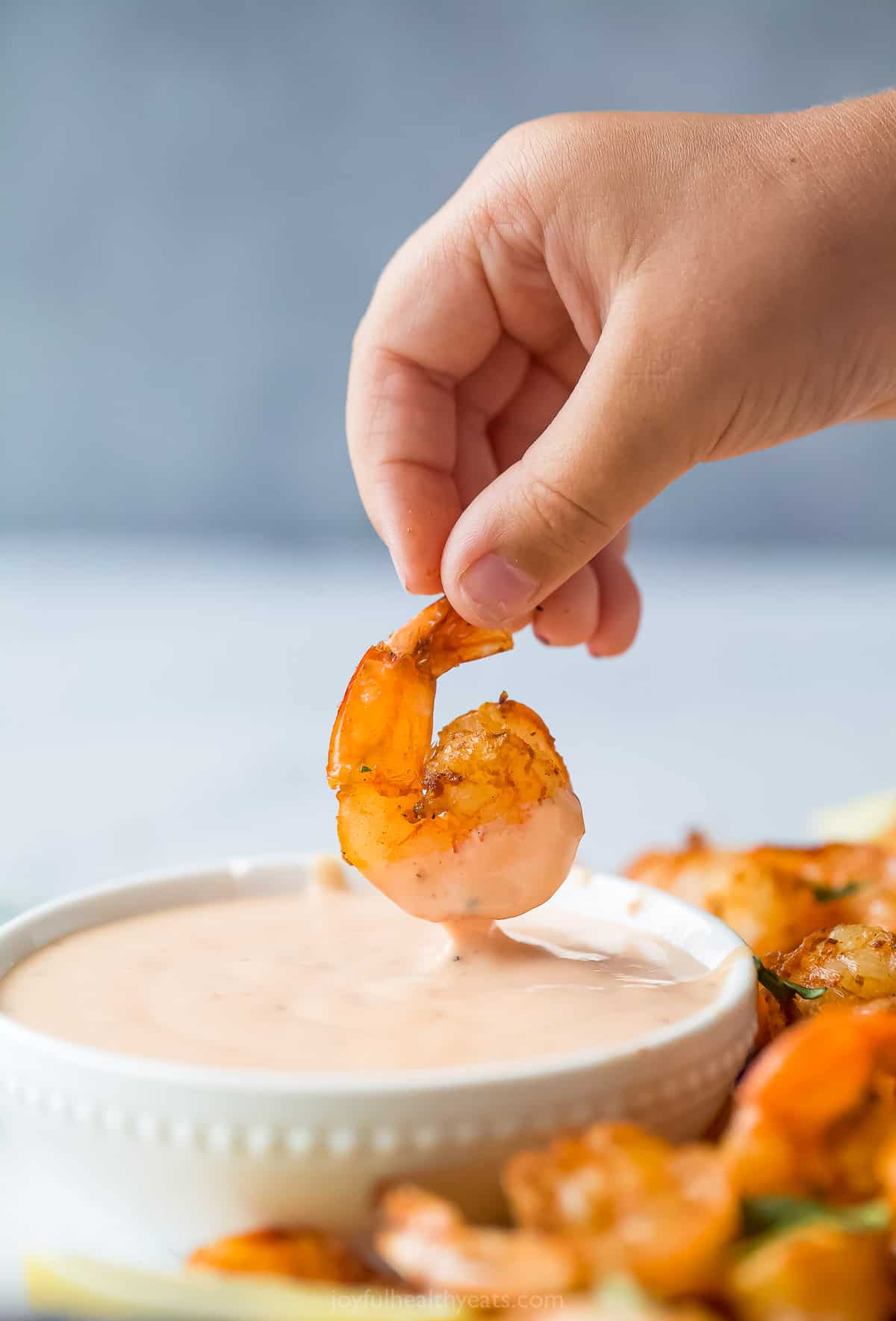 someone dipping shrimp into a pale red dipping sauce