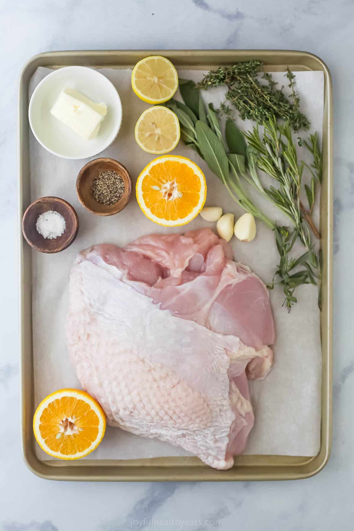 sheet pan with raw turke breast, orange halves, lemon halves, herbs, salt, pepper and butter