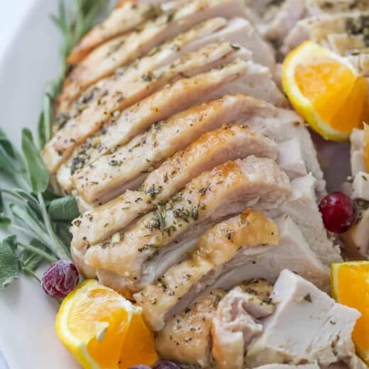 roasted turkey breast that's been sliced on a plate with herbs and orange wedges