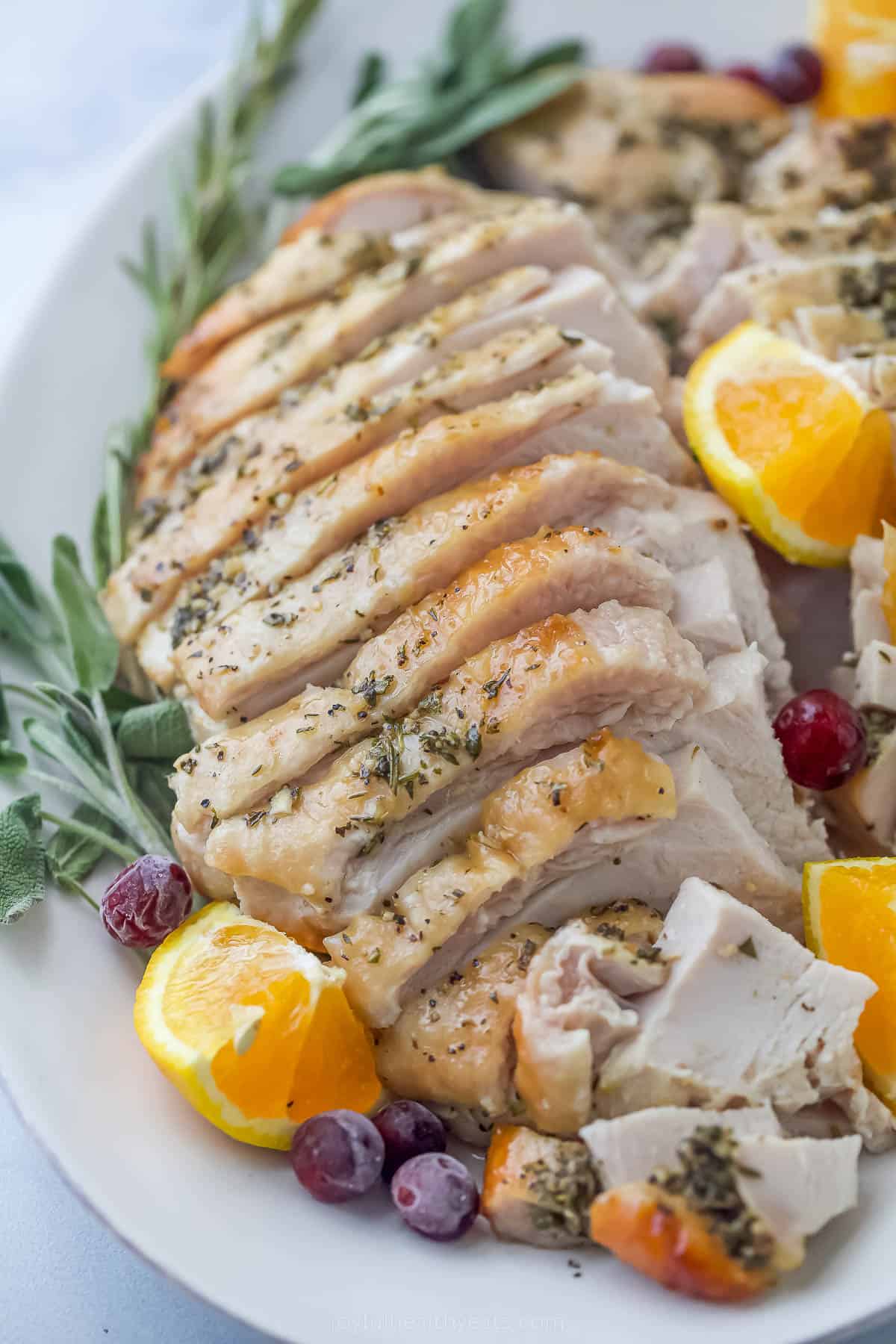 roasted turkey breast that's been sliced on a plate with herbs and orange wedges