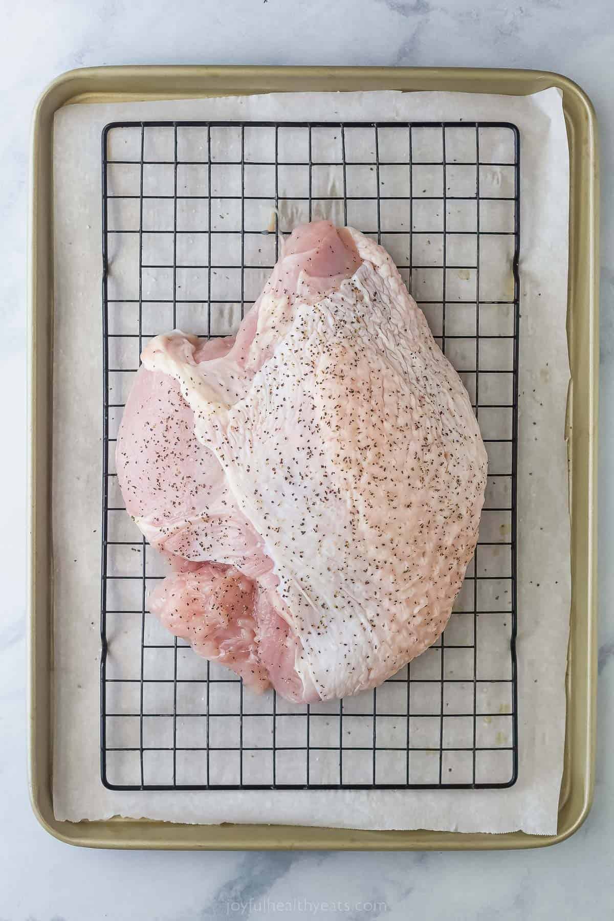 a raw turkey breast on a baking rack seasoned with salt and pepper