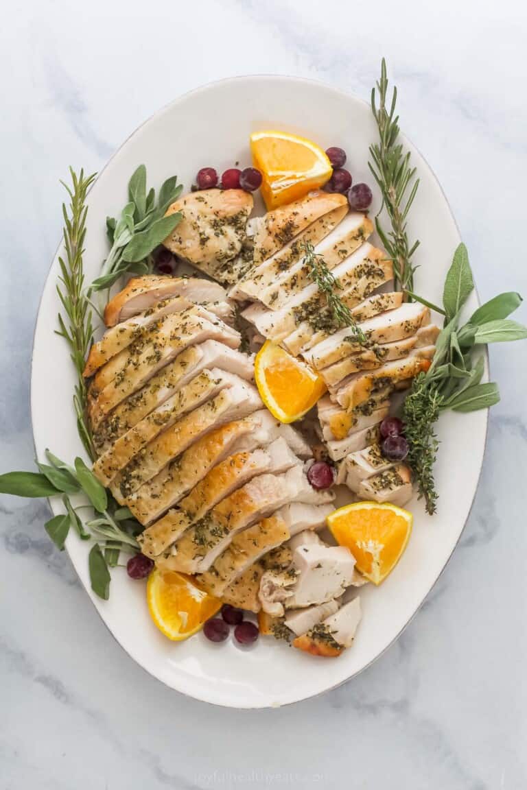 roasted turkey breast that's been sliced on a plate with herbs and orange wedges