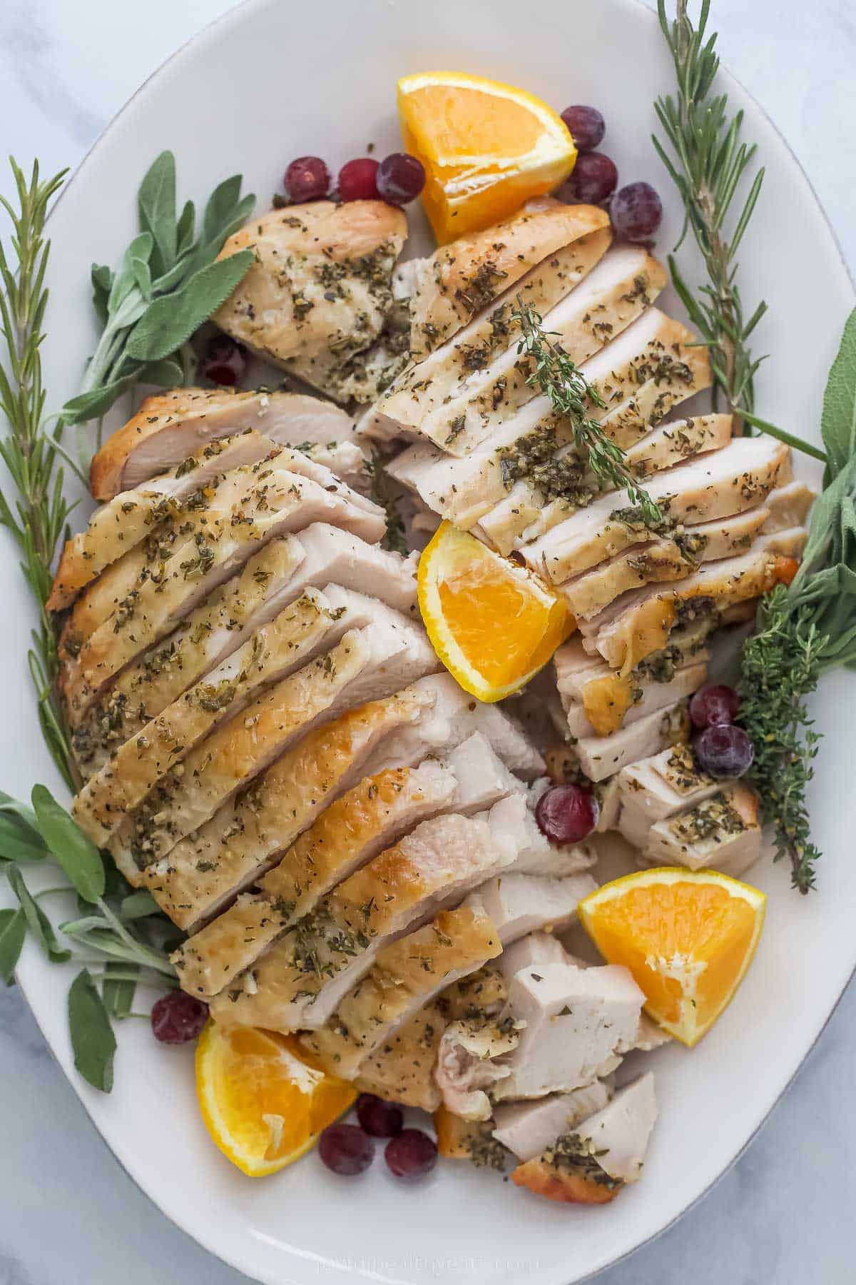 roasted turkey breast that's been sliced on a plate with herbs and orange wedges