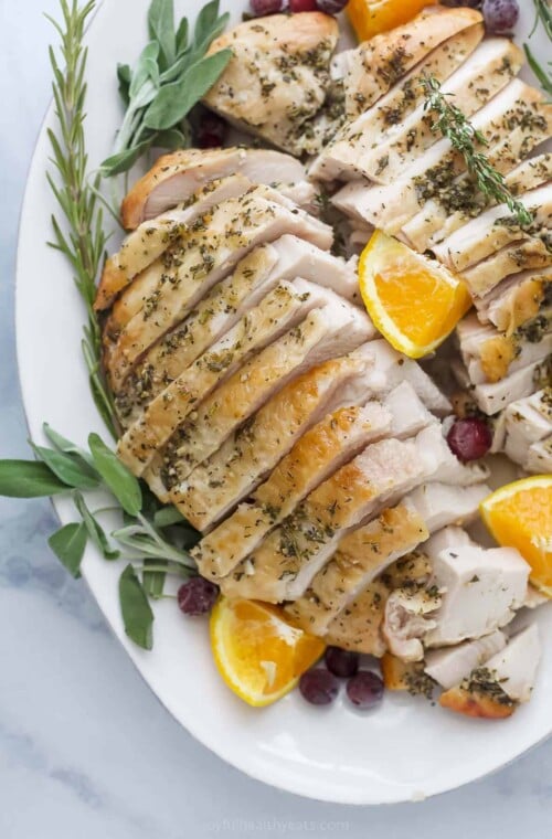 roasted turkey breast that's been sliced on a plate with herbs and orange wedges